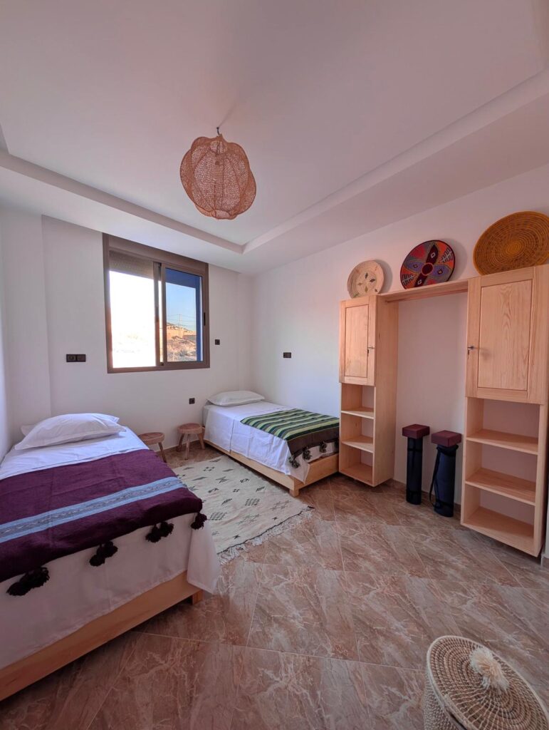 Surf camp in Morocco for solo travellers: What to look for before booking 2 Twin shared room in The Happy Surfers surf camp in Tamraght, Morocco, with two beds, window, and cozy furniture