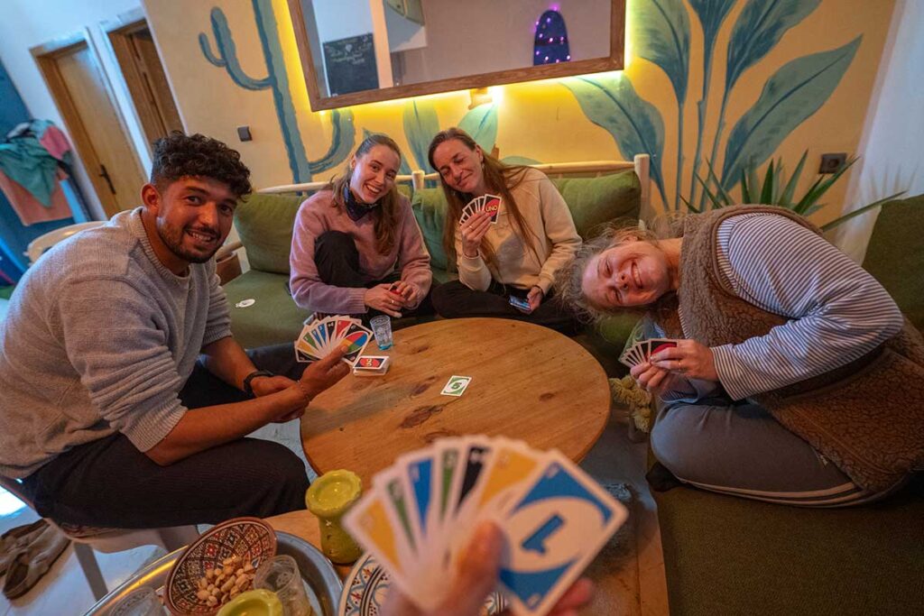 Is an All-Inclusive Surf Camp in Morocco worth it? Costs, inclusions and who it suits 4 Guests relaxing and playing Uno with a surf instructor in the chill area at The Happy Surfers surf camp in Tamraght