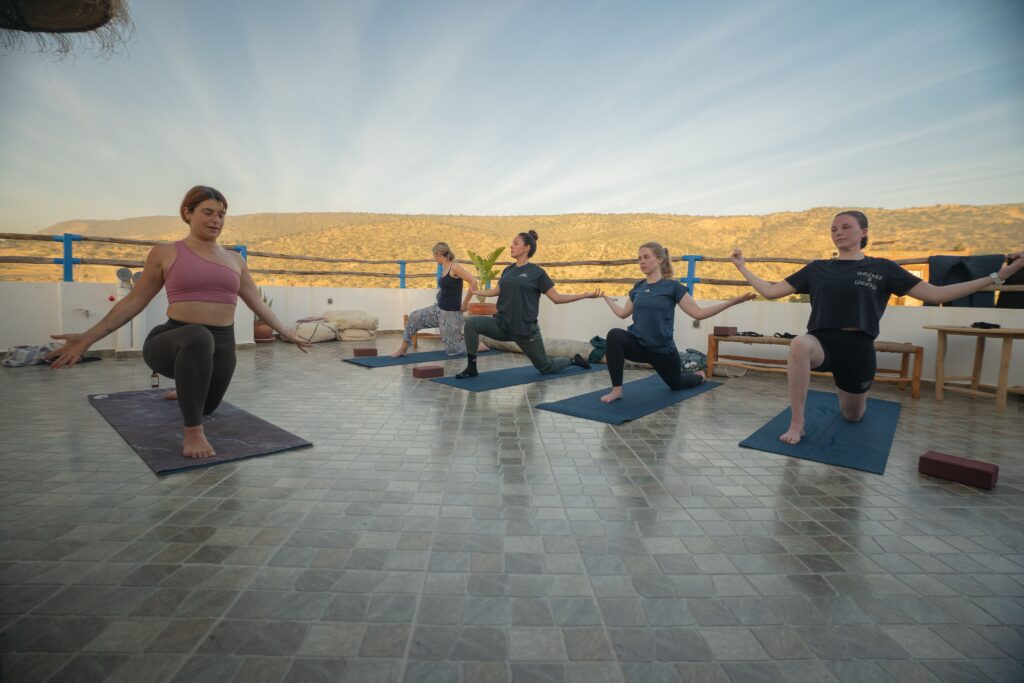 What to wear in Morocco as a Woman: A Practical Guide for Tamraght and surf towns 3 Women practising yoga in activewear on a rooftop terrace at sunrise in Tamraght